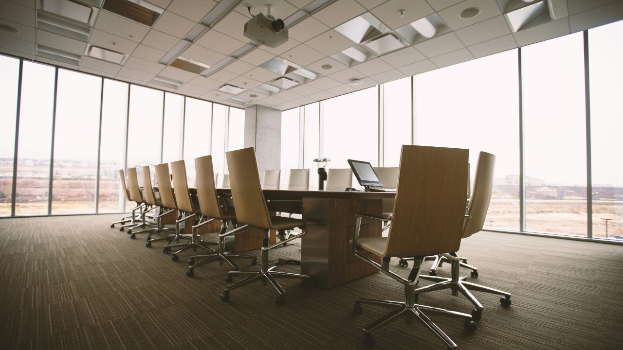 An empty corporate boardroom with a long table, executive chairs, and floor-to-ceiling windows