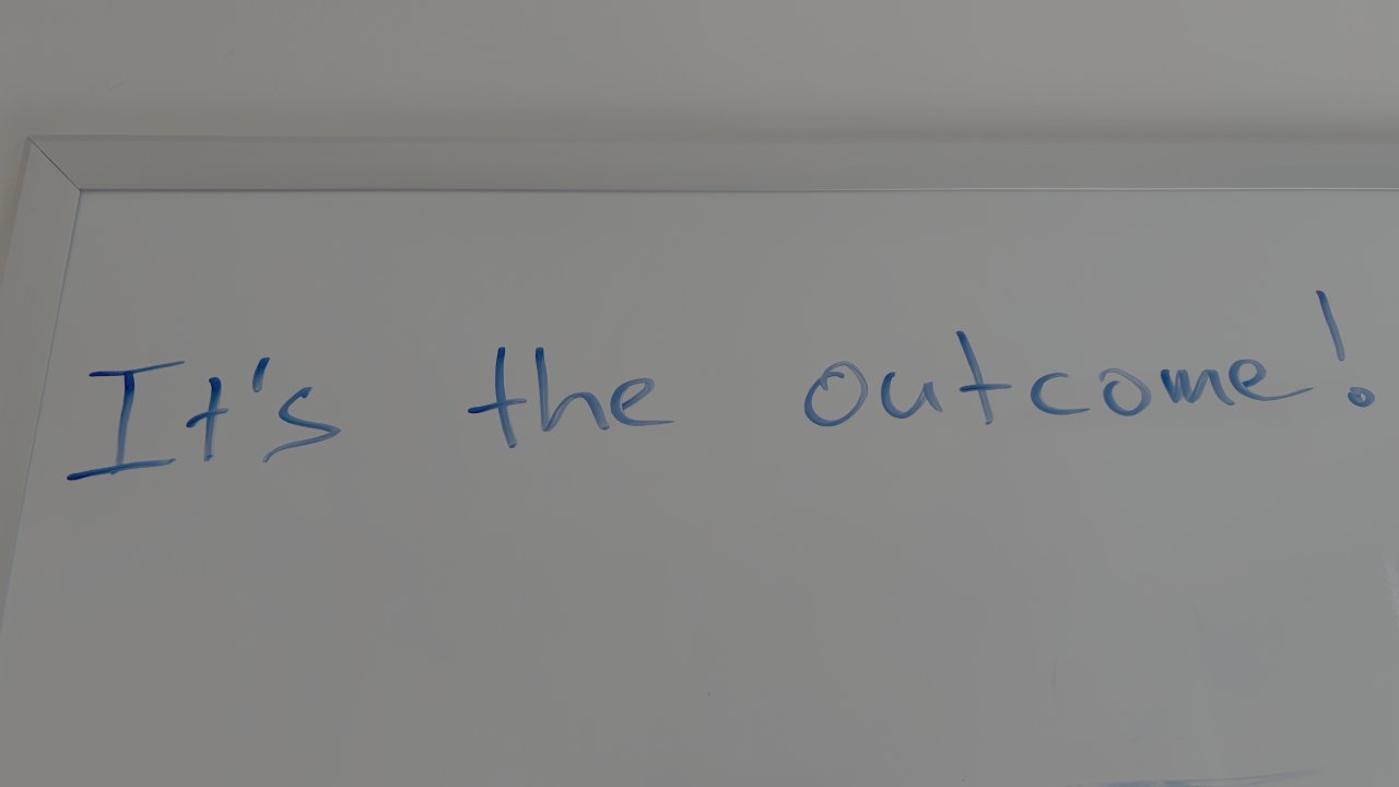 A whiteboard with the handwritten words 'It's the outcome!' in blue marker